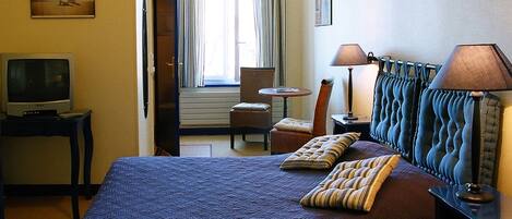 Una habitación de hotel con cama, televisión, silla, mesa y ventana con cortinas.
