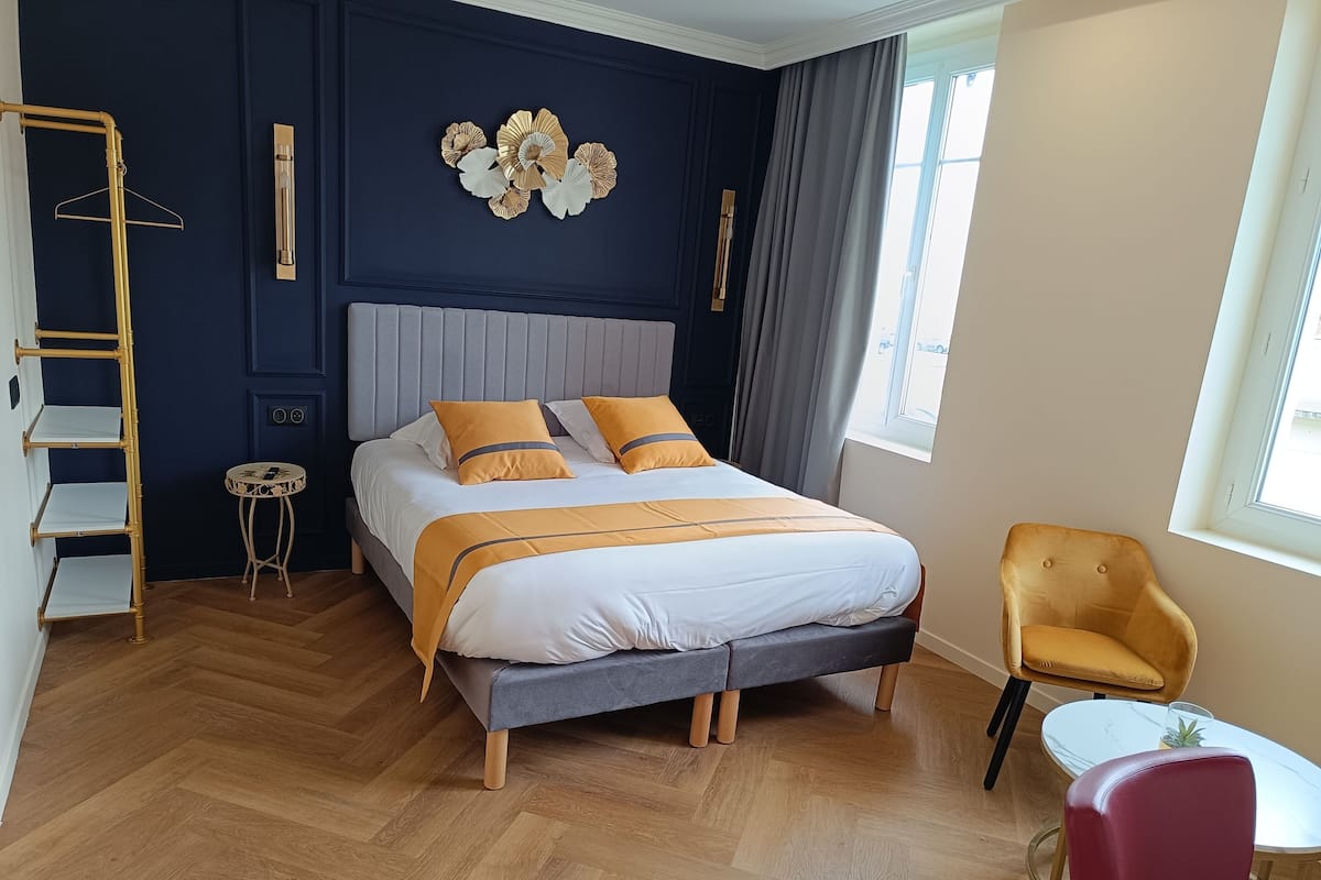 A modern bedroom with a bed, a chair, a small table, a ladder, and a decorative wall piece.