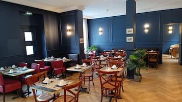 Un restaurante con mesas y sillas de madera, paredes oscuras y luces fijadas a la pared.