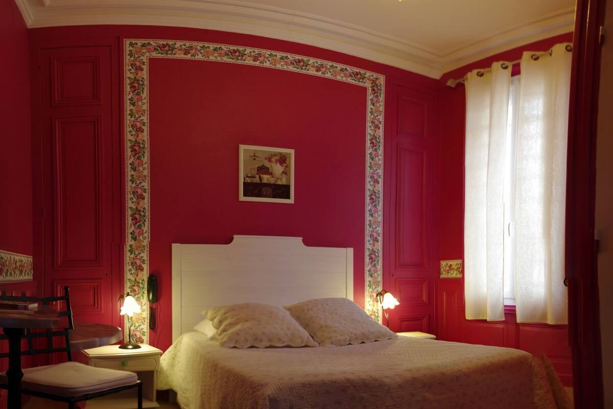 A bedroom with a large bed, two bedside tables with lamps, a chair, and a window with curtains.