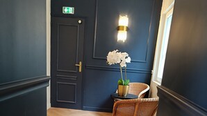 A hallway with a dark door, a wicker chair, and a small table with a potted plant. - The Originals Boutique, Hôtel d'Angleterre, Fécamp (Fecamp)