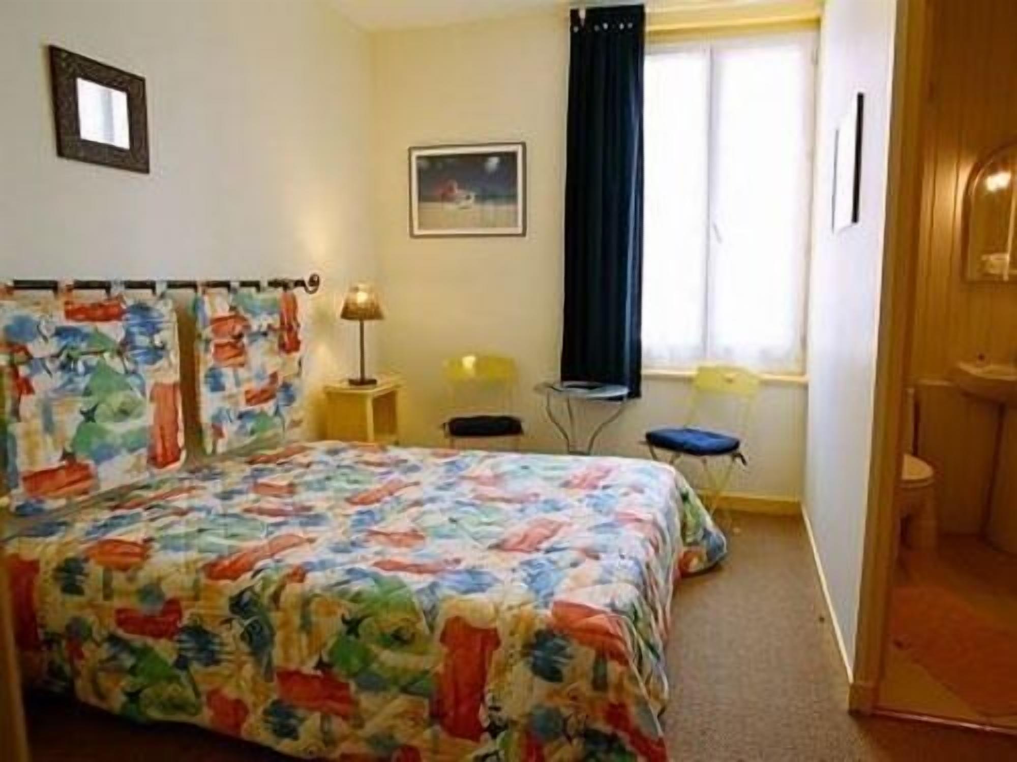 Un dormitorio con cama, mesita de noche, silla, ventana con cortinas y puerta.