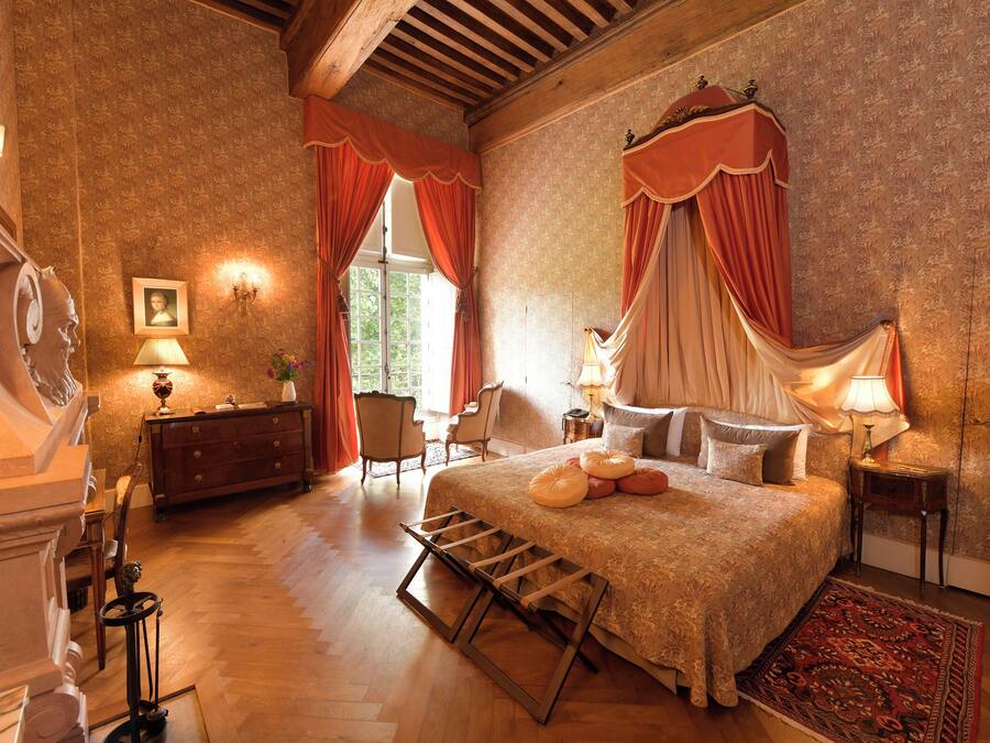 A bedroom with a large bed, a wooden floor, a dresser, a chair, and a window with curtains.