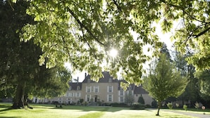 Un grand bâtiment historique à la façade symétrique, entouré de pelouses bien entretenues et d’arbres majestueux.