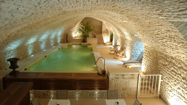 Une piscine intérieure dotée d’un plafond en pierre, entourée d’espaces aménagés pour s’asseoir et de plantes en pot.