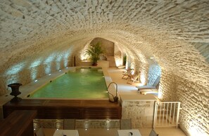 An indoor swimming pool with a stone ceiling, surrounded by seating areas and potted plants.