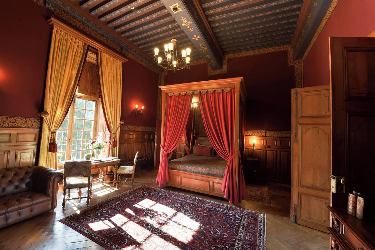 Ein Schlafzimmer mit einem Himmelbett, einem großen, verzierten Teppich und einer Kristallleuchtre.