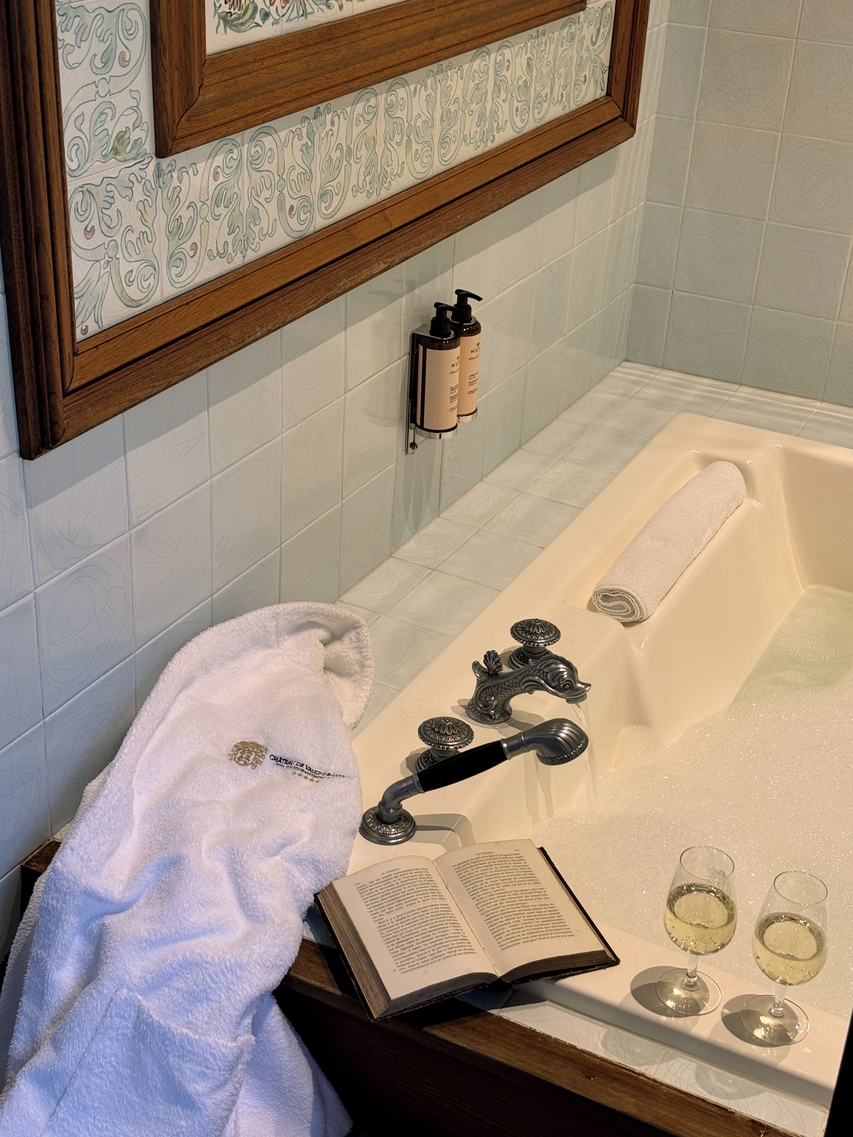 A bathroom with a bathtub, a towel, an open book, and two glasses of water.