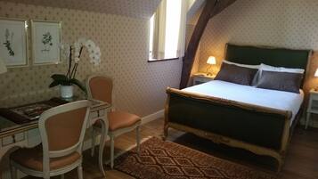 A bedroom with a bed, a desk with a chair, a nightstand, a lamp, and a window with curtains.