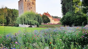 Uma torre de pedra histórica com telhado vermelho, rodeada por um jardim exuberante cheio de flores coloridas.