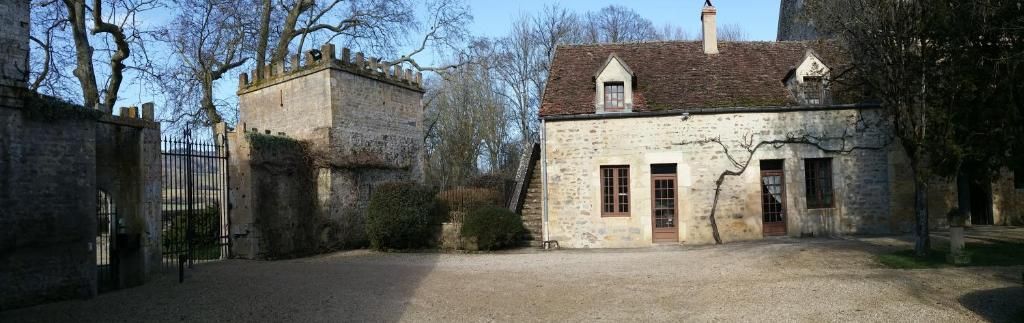 Un bâtiment en pierre avec une allée gravillonnée et une entrée fermée par un portail.