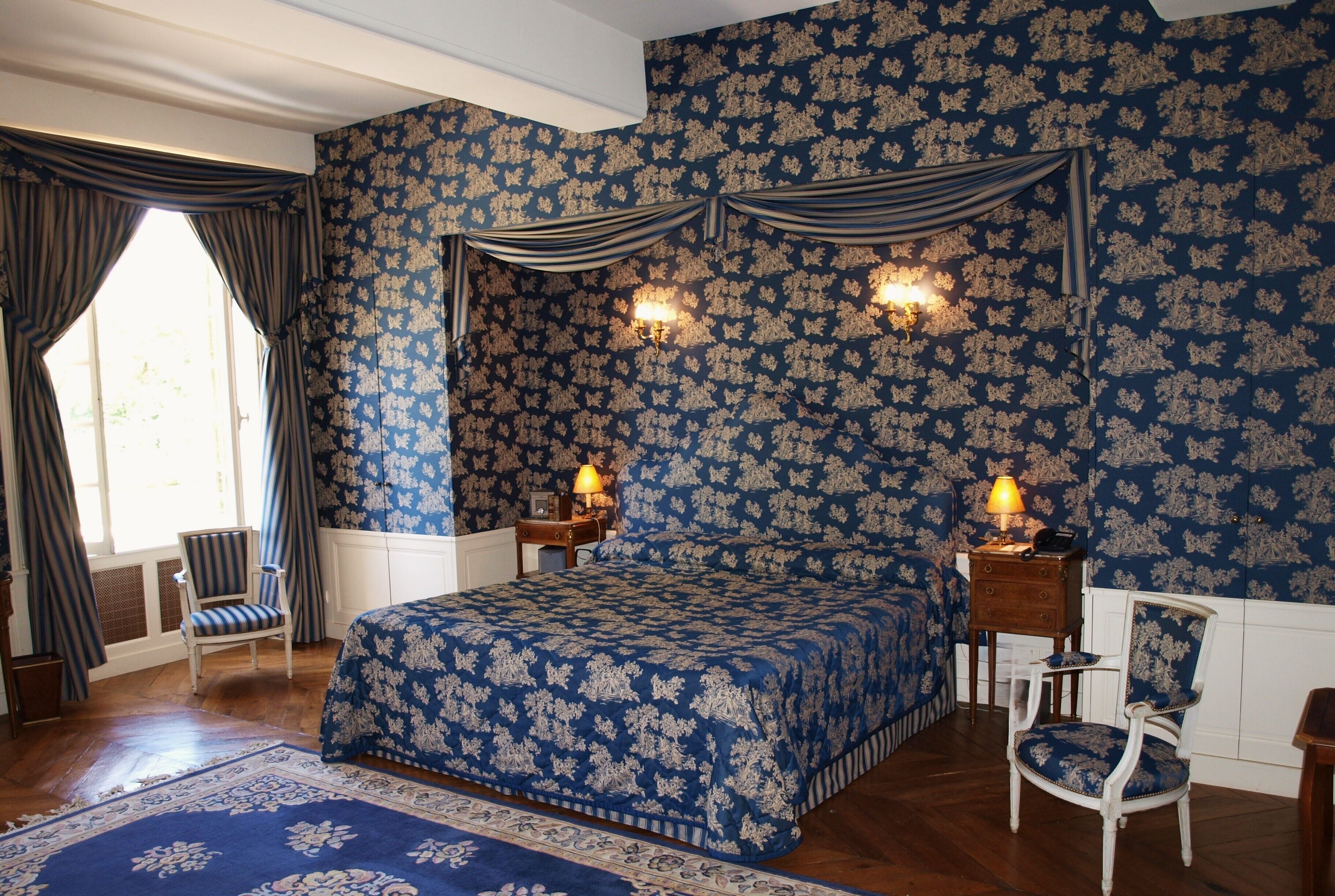 A bedroom with a large bed, two wall sconces, a chair, and a nightstand.