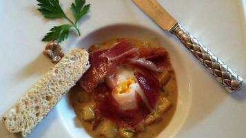 A bowl of soup with a poached egg, prosciutto, and bread on a white plate.