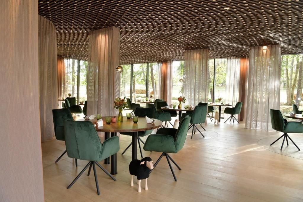 Un comedor con mesas redondas, sillas tapizadas en verde y un techo de madera.