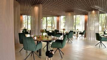 Un comedor con mesas redondas, sillas tapizadas en verde y un techo de madera.