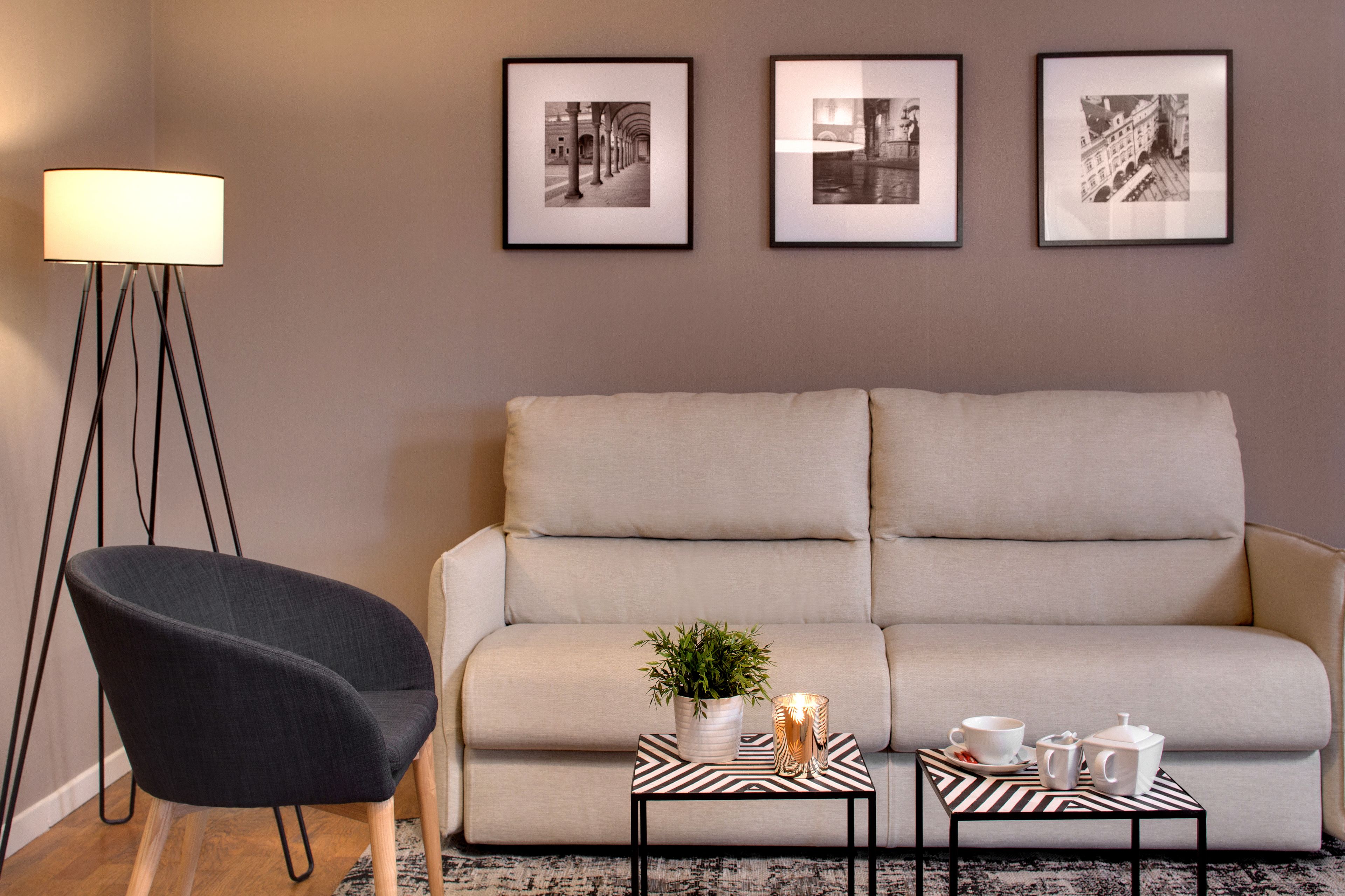Un salon avec un canapé, un fauteuil, une petite table sur laquelle est posée une plante, et des tableaux encadrés accrochés au mur.