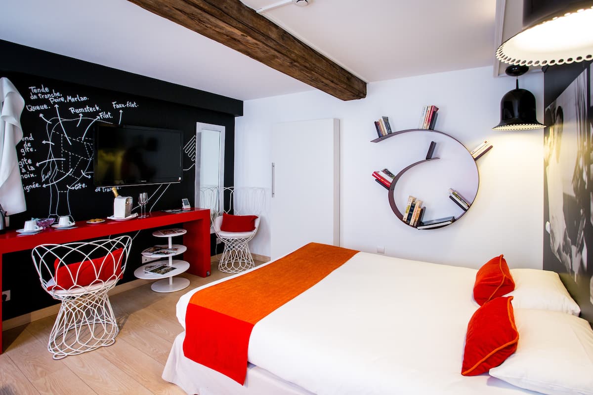 A modern hotel room with a bed, a desk, a chair, a round mirror, and a wall with a chalkboard.