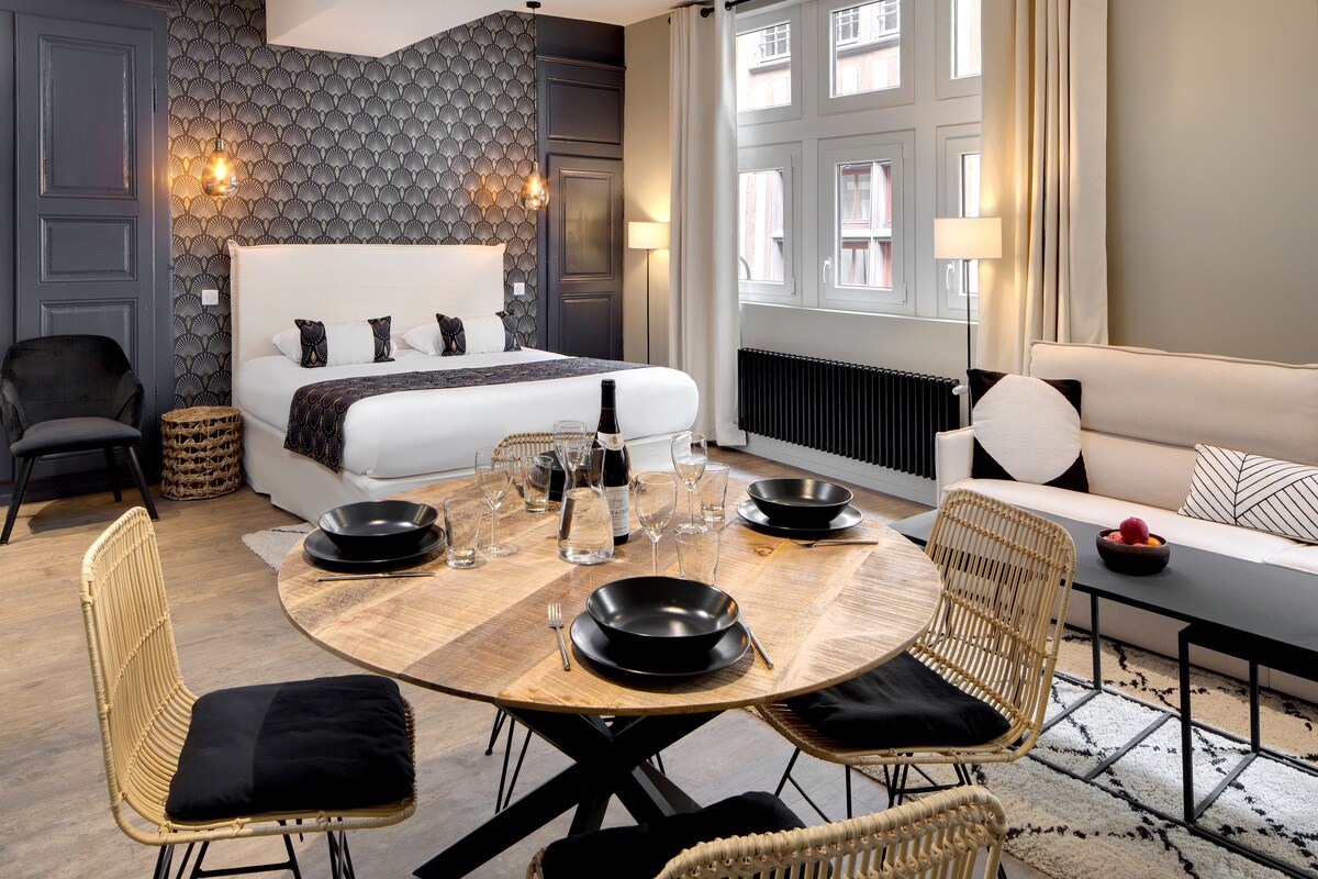A modern hotel room with a large bed, a dining table set for four, and a sofa.