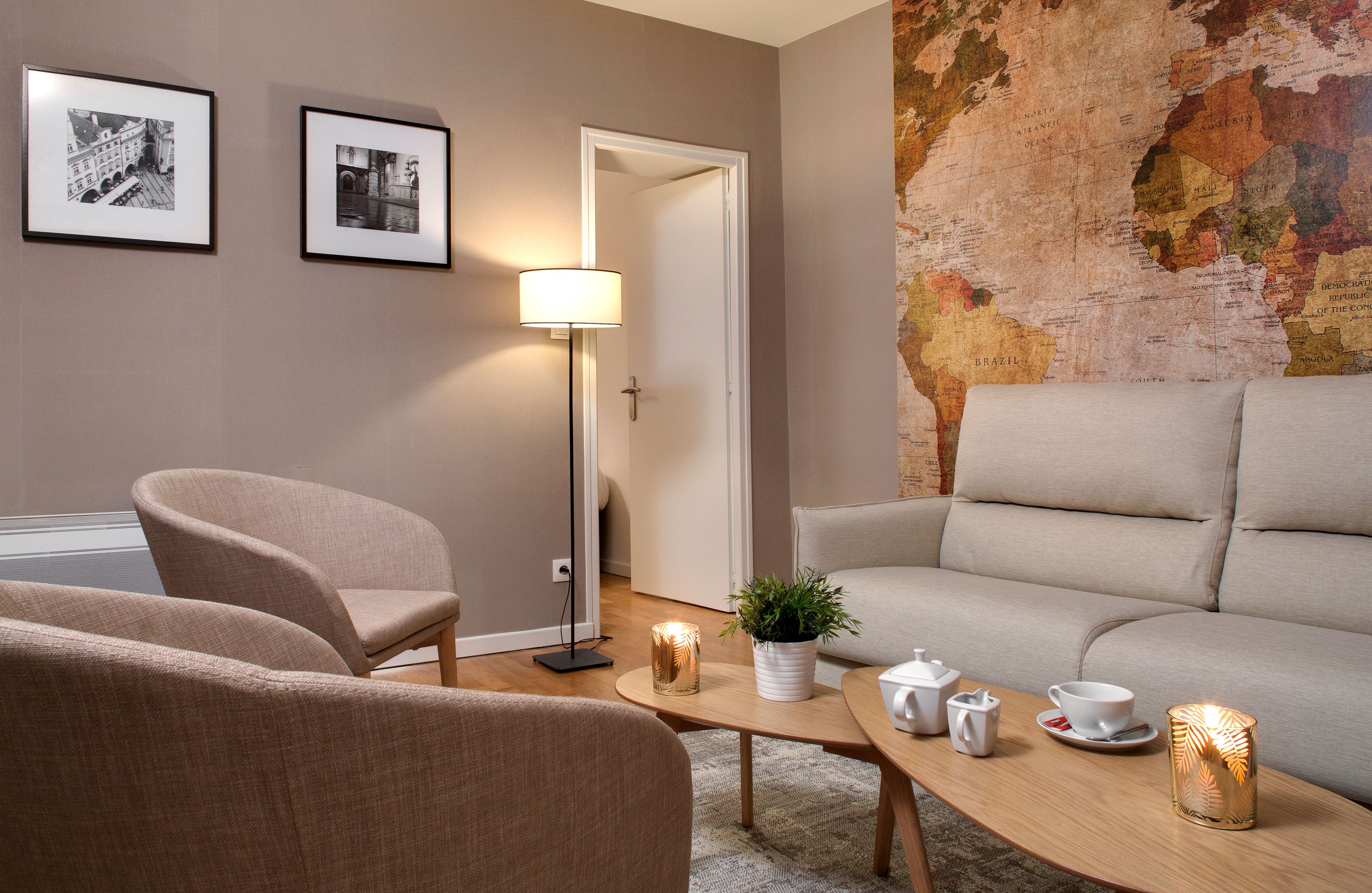 A modern living room with a sofa, armchairs, a coffee table with tea set, and a map on the wall.