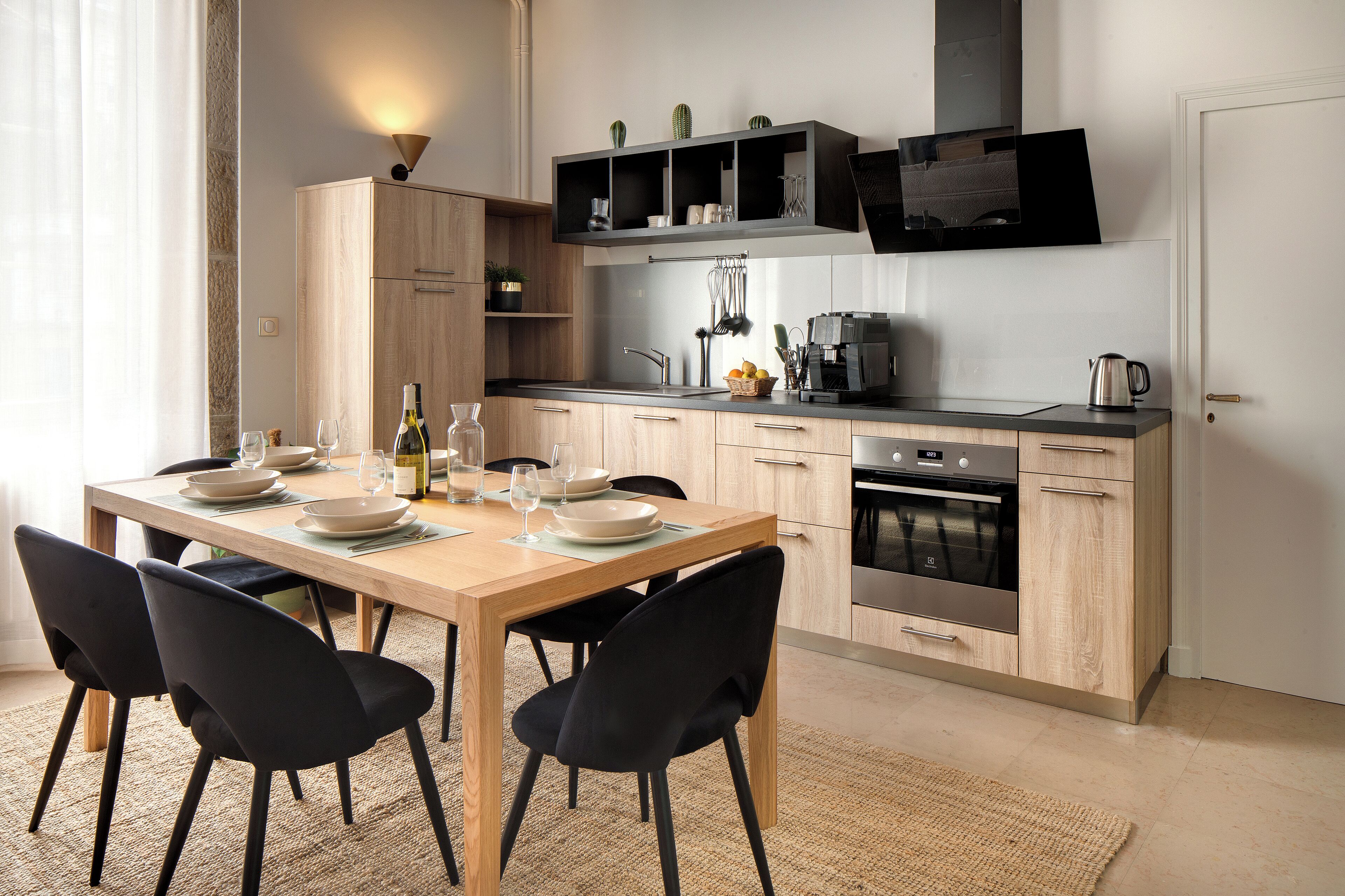 A modern kitchen with a wooden table set for dining, black chairs, and a built-in oven.