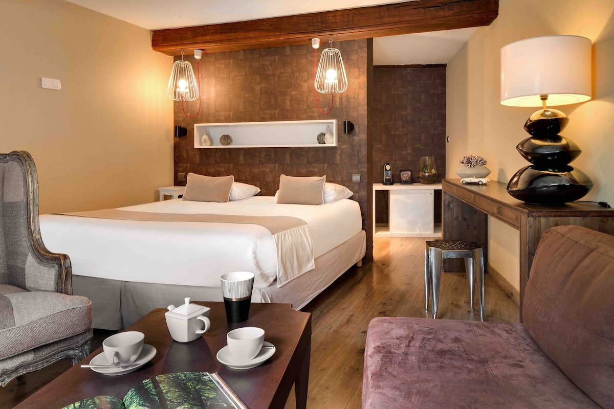 A hotel room with a large bed, two bedside tables, a desk, a chair, and a sofa.