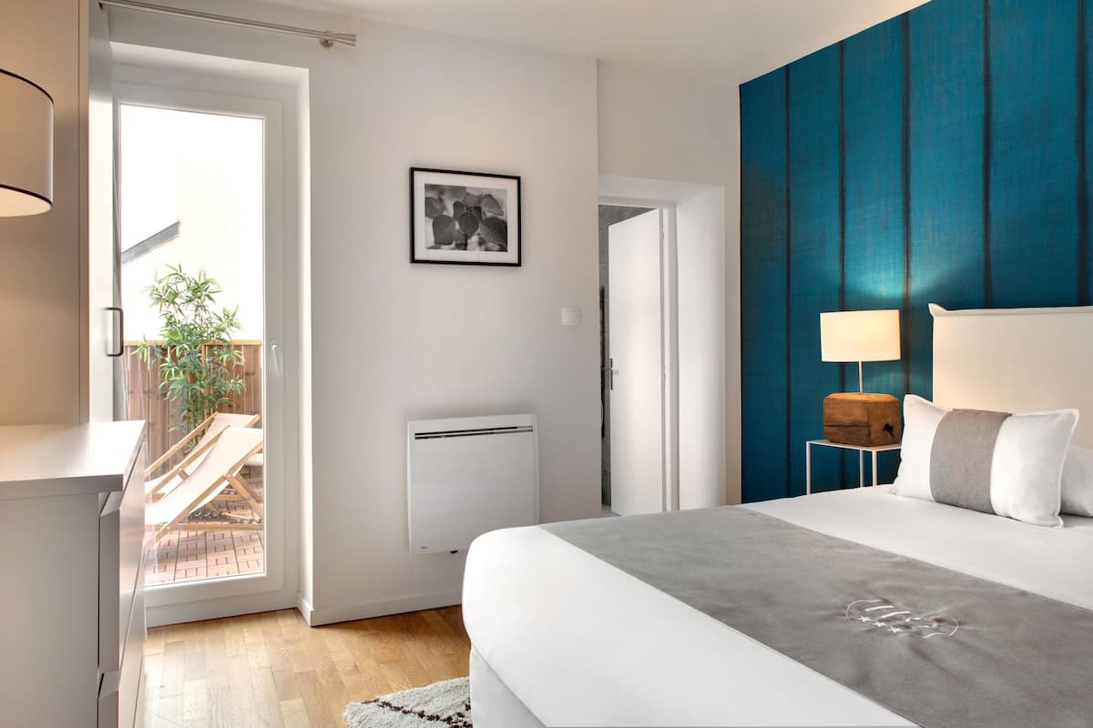 A bedroom with a bed, a bedside table, a lamp, a picture on the wall, and a view of a balcony.