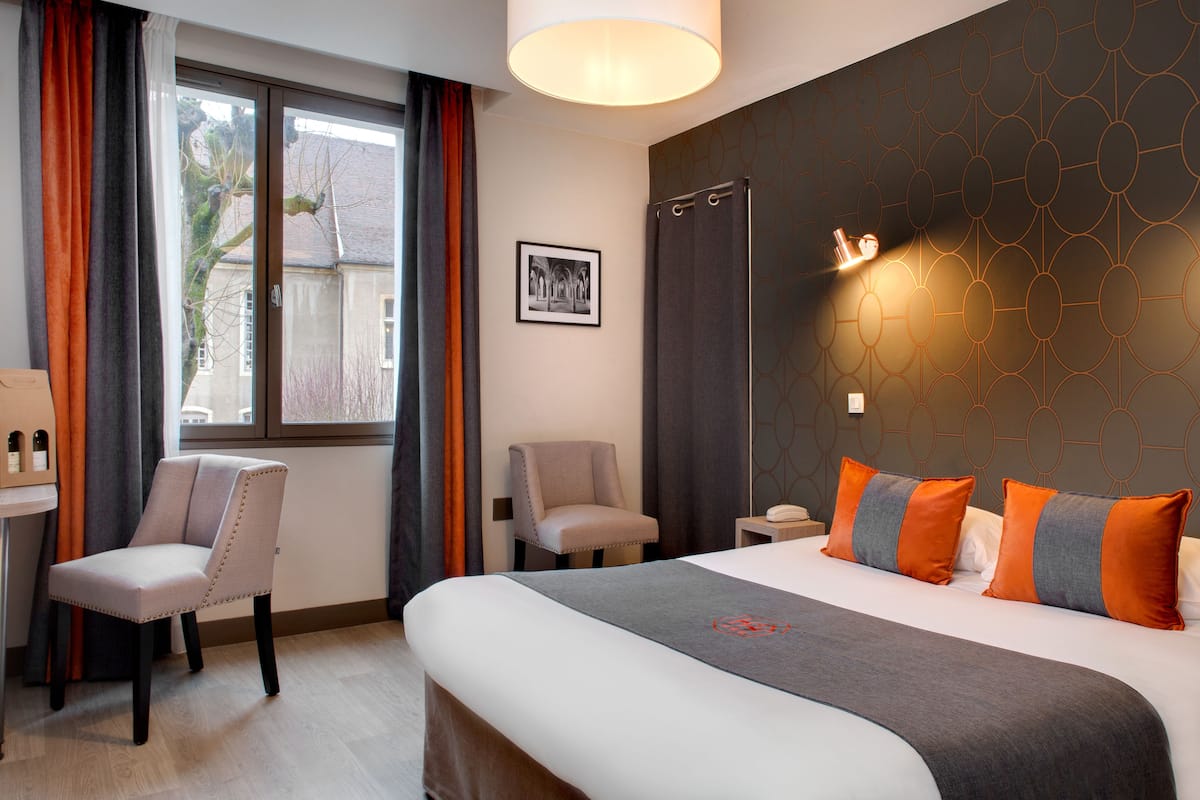 A hotel room with a bed, two chairs, a desk, and a window with curtains.