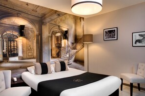 A luxurious hotel room with a large bed, a chair, a desk, and a staircase leading to an upper level. - Hôtel des Ducs (Dijon)