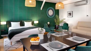 Une chambre d’hôtel moderne avec un lit soigneusement fait, une table à manger dressée pour deux personnes et un canapé recouvert d’un tissu vert.