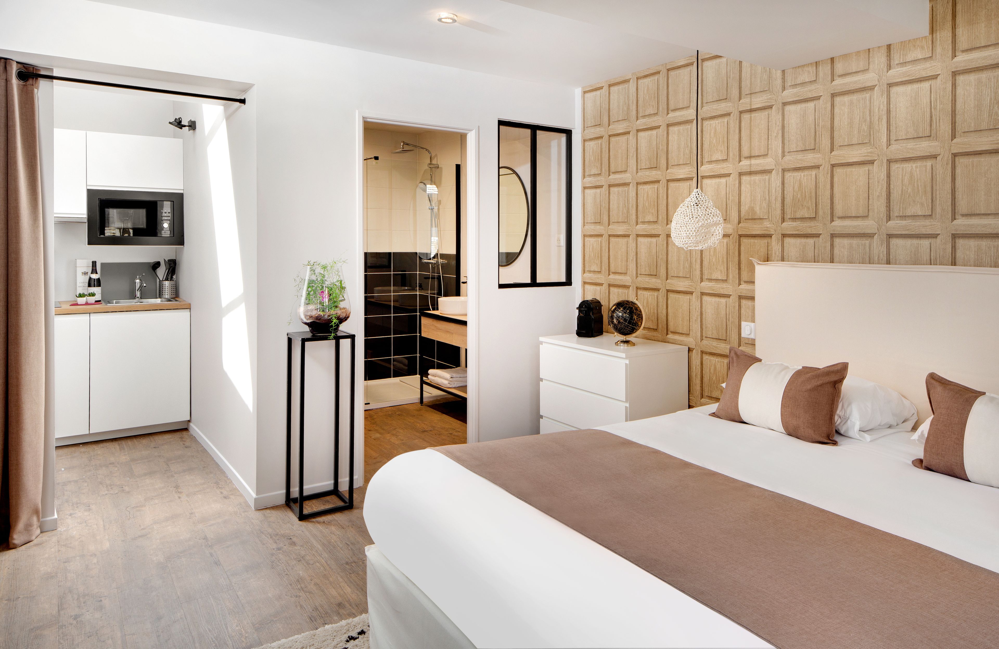 A modern hotel room with a large bed, a bedside table, a small desk, a microwave, a sink, and a shower.