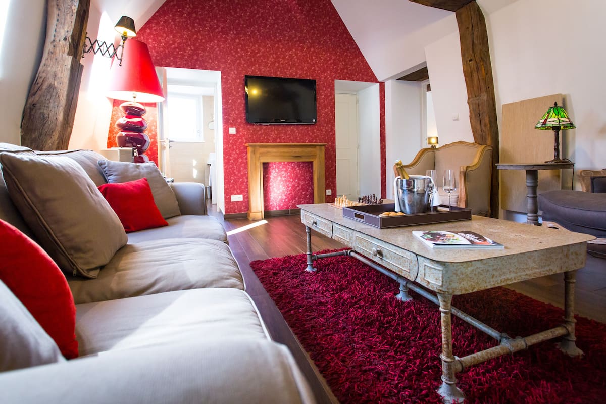 A living room with a red carpet, a fireplace, a television, and a sofa with red cushions.