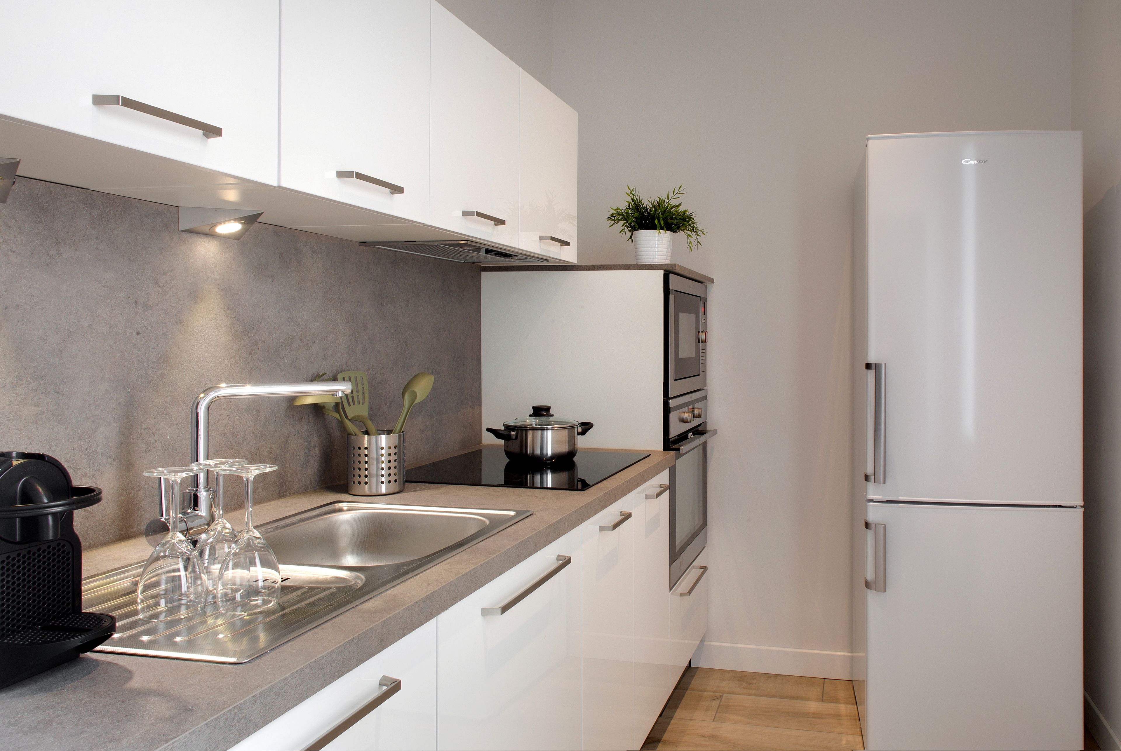 Una cocina moderna con armarios blancos, un lavamanos de acero inoxidable, horno empotrado y refrigerador.