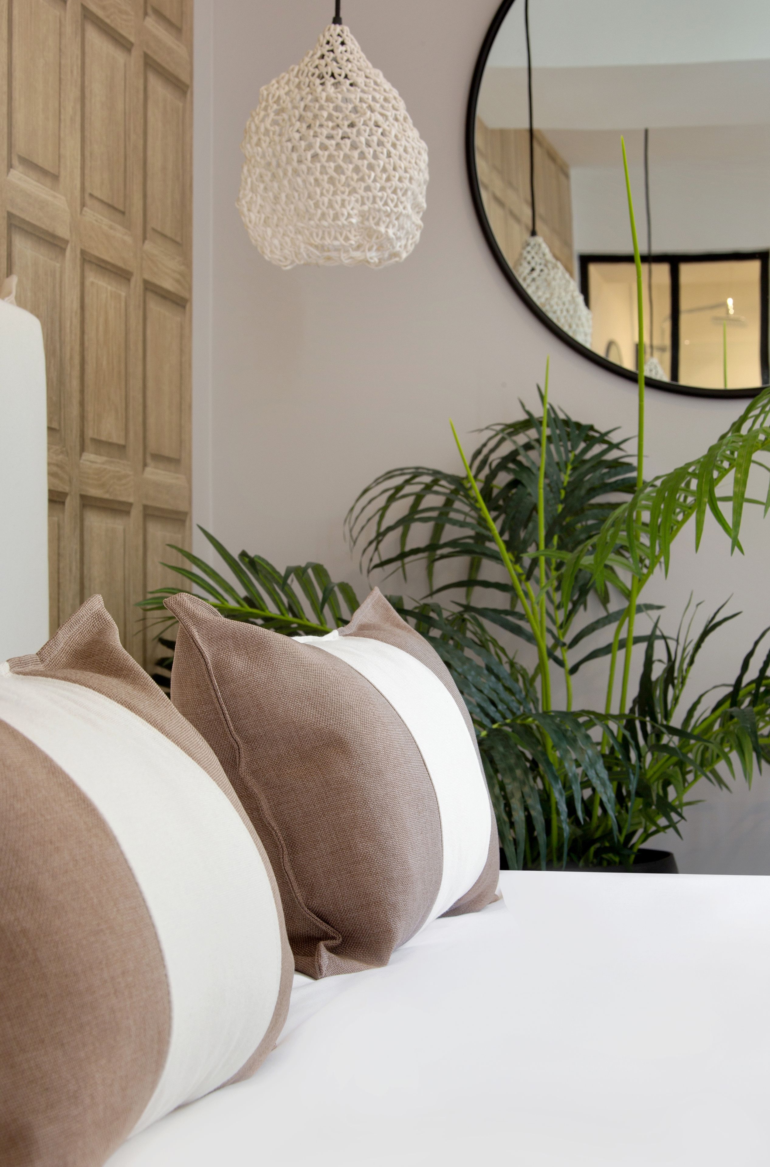 A bedroom with a bed, a hanging light fixture, a mirror, and a potted plant.