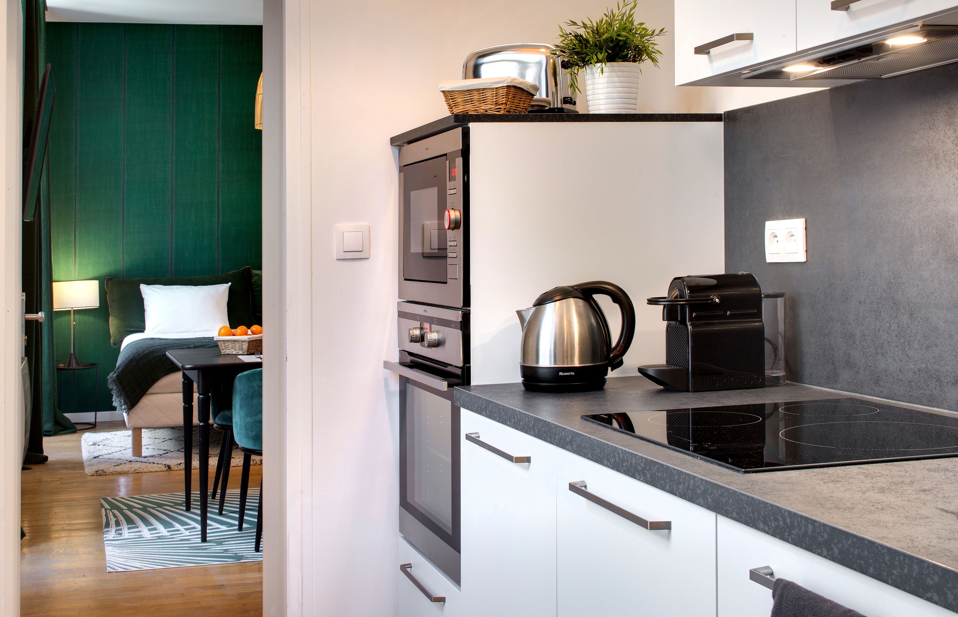 A compact kitchen with a built-in oven, a coffee maker, and a kettle on the countertop.