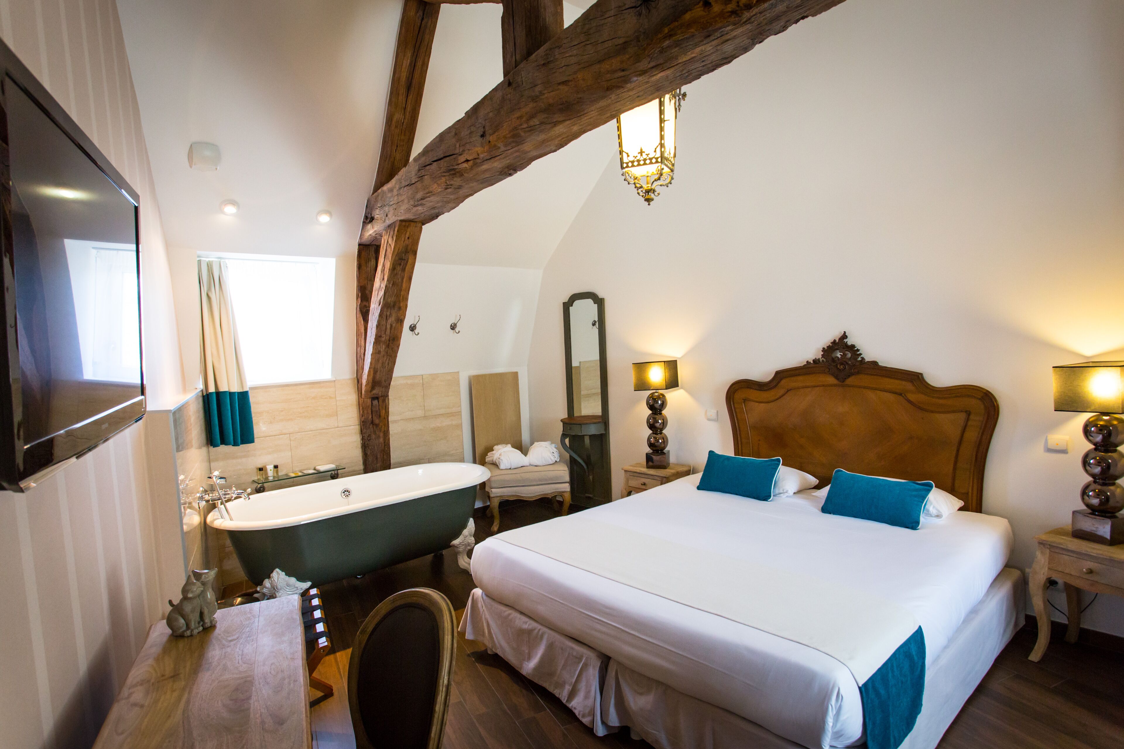 Une chambre avec un grand lit, une baignoire, une poutre en bois au plafond, un miroir et un téléviseur fixé au mur.