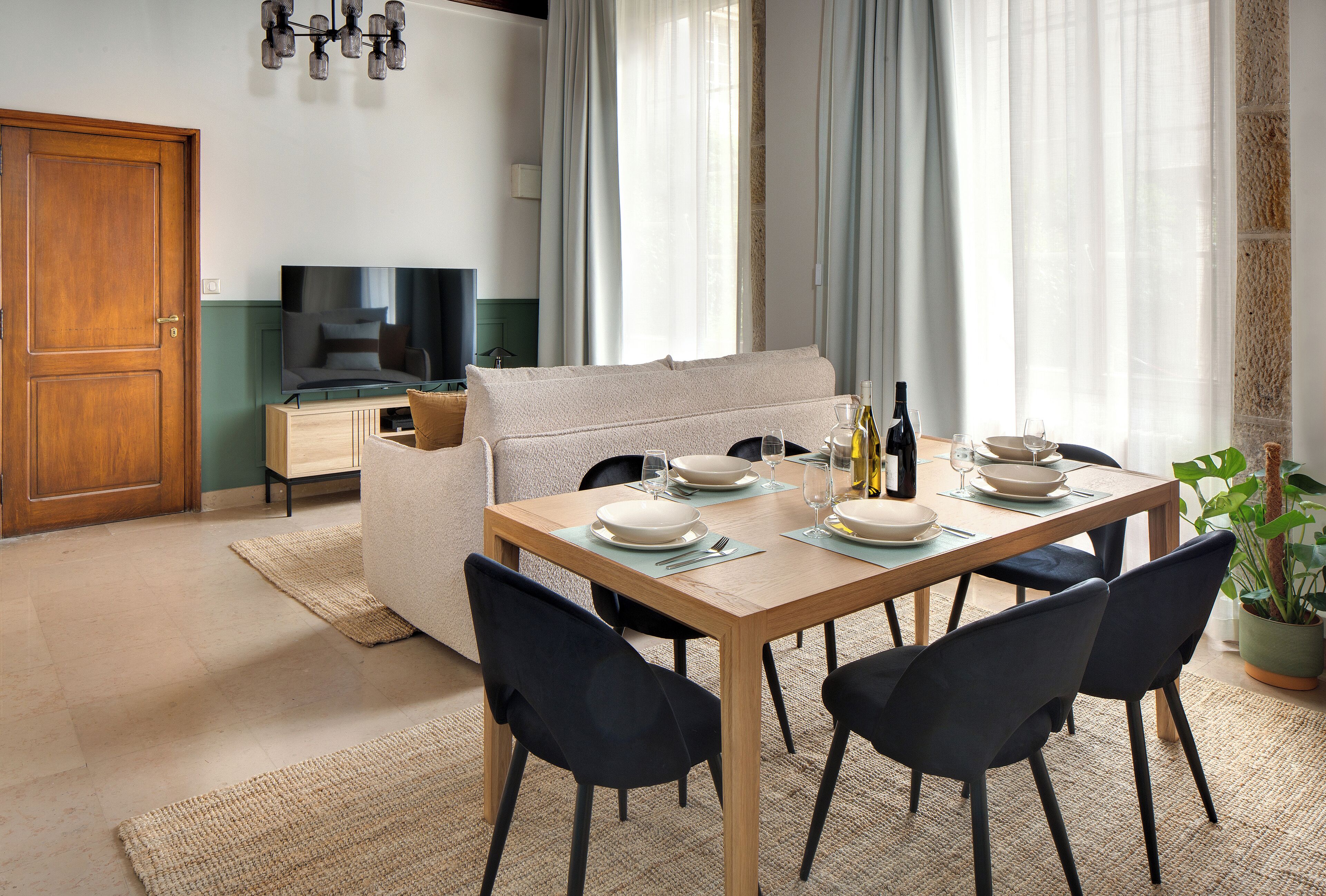 A dining area with a wooden table set for four, a sofa, and a television in the background.