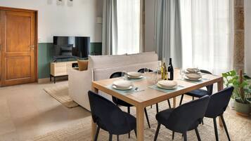 A dining area with a wooden table set for four, a sofa, and a television in the background.