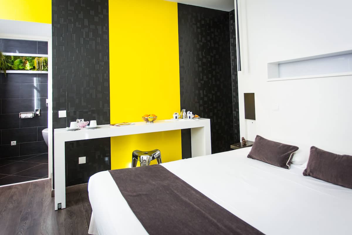 A modern hotel room with a large bed, a desk, and a small seating area.
