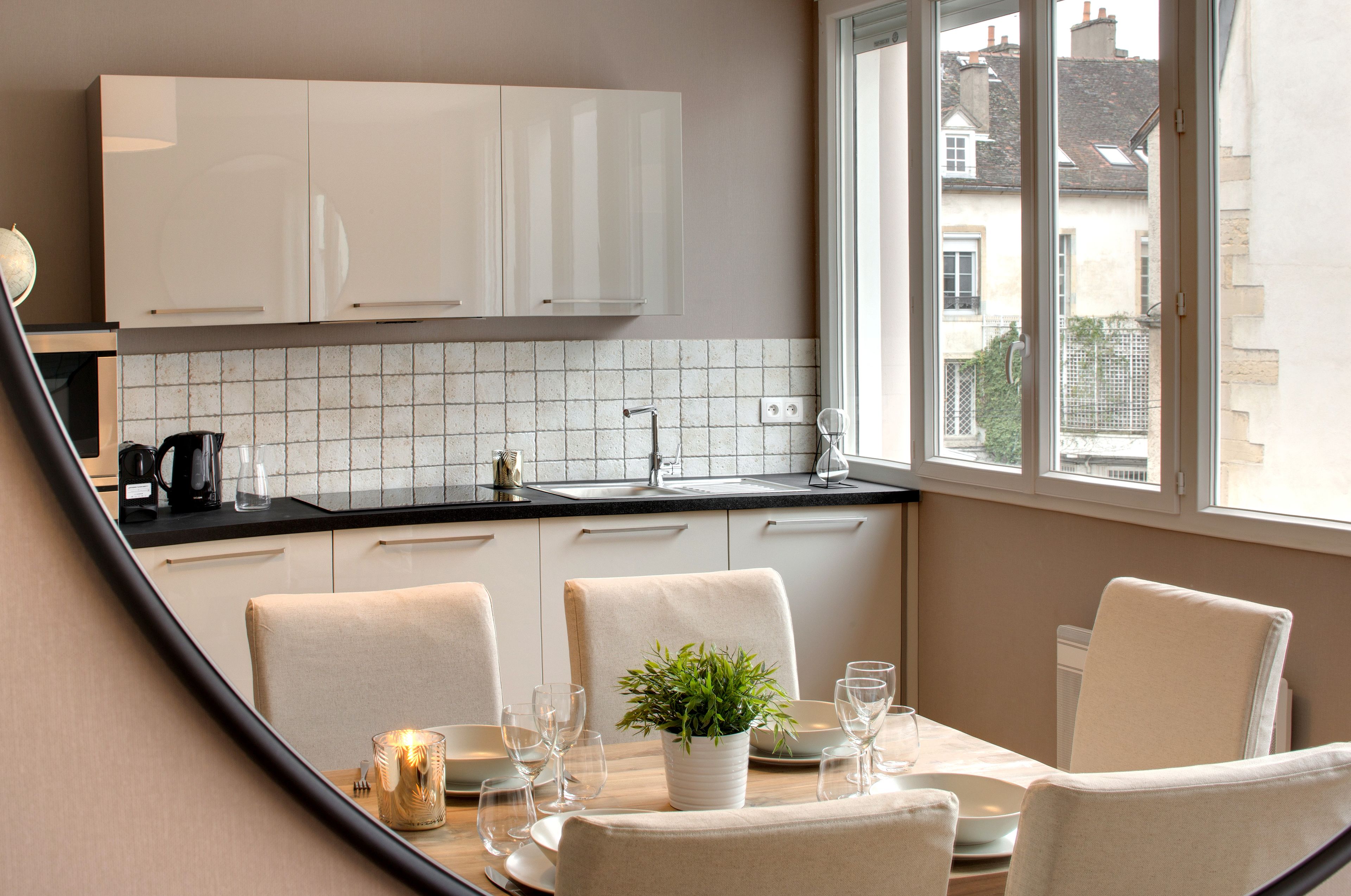 A modern kitchen with white cabinets, a tiled backsplash, and a dining area with a table set for four.