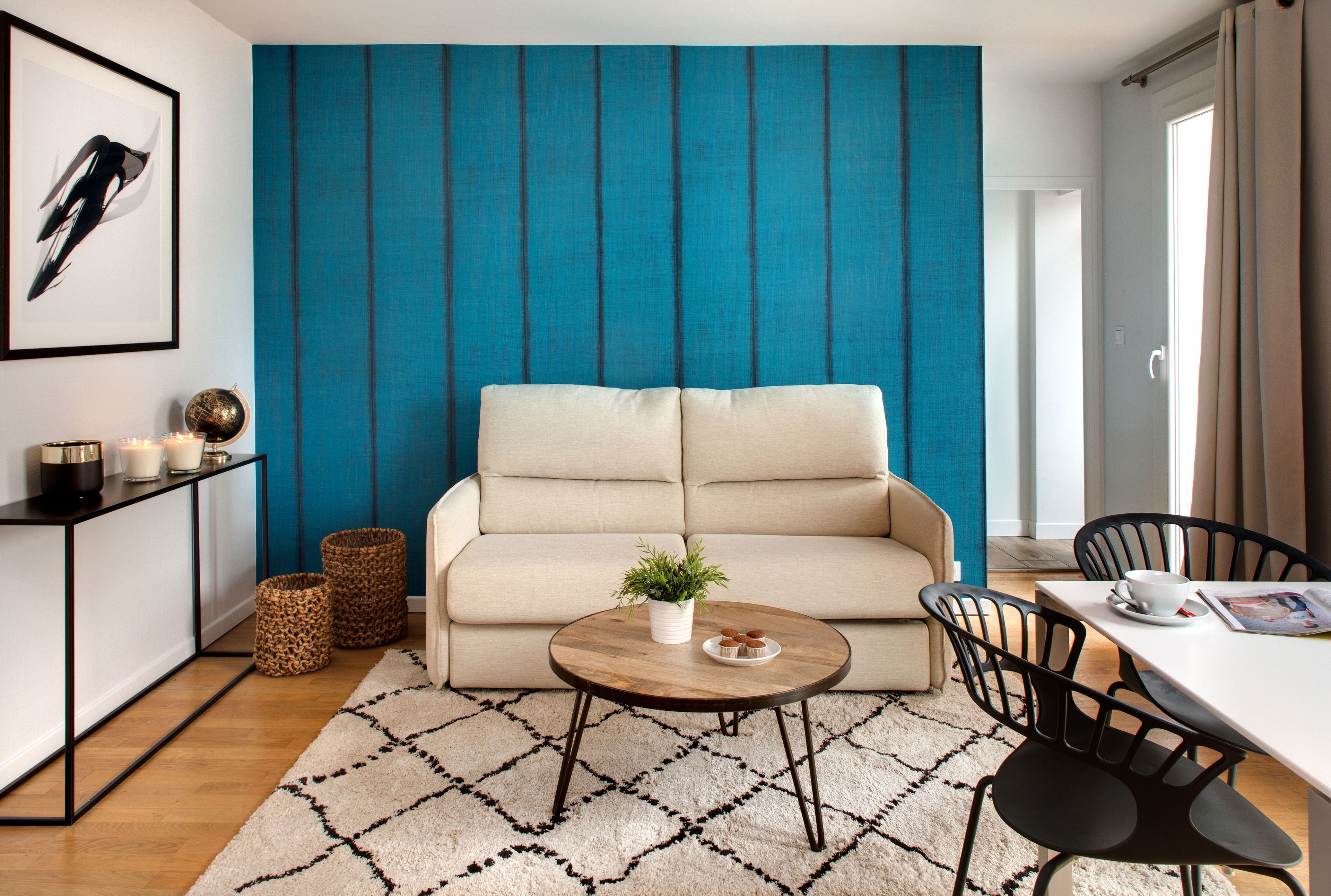 Una sala moderna con un sofá color beige, una mesa de centro redonda de madera y una pequeña planta en maceta.