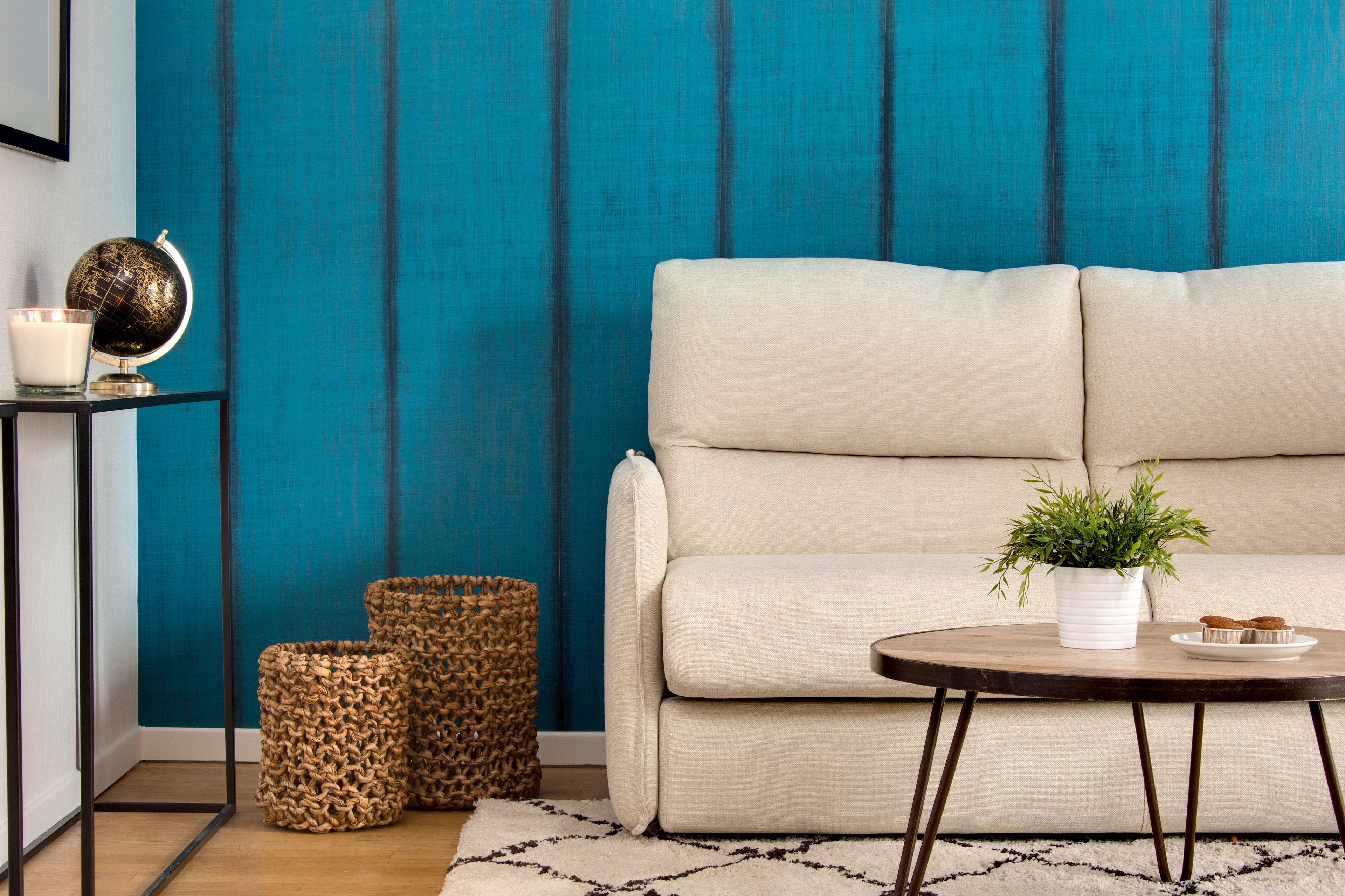 A modern living room with a teal accent wall, a beige sofa, a round coffee table with a plant, and wicker baskets.