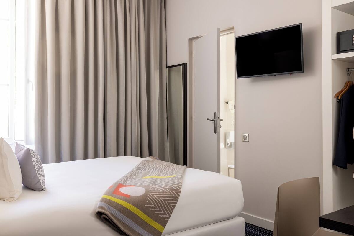 Hotellihuone, jossa on sänky, seinälle asennettu televisio, ovi ja naulakko.
