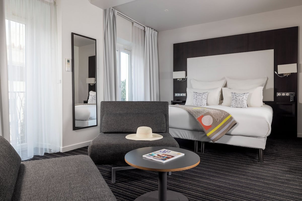 Hotellihuone, jossa on sänky, tuoli, pieni pöytä ja peili.