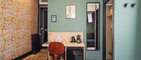 A hotel room with a bed, a desk, a chair, a radiator, a mirror, and a door.