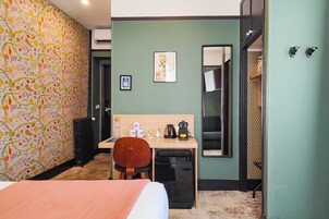 Une chambre d’hôtel avec un lit, un bureau, une chaise, un radiateur, un miroir et une porte.