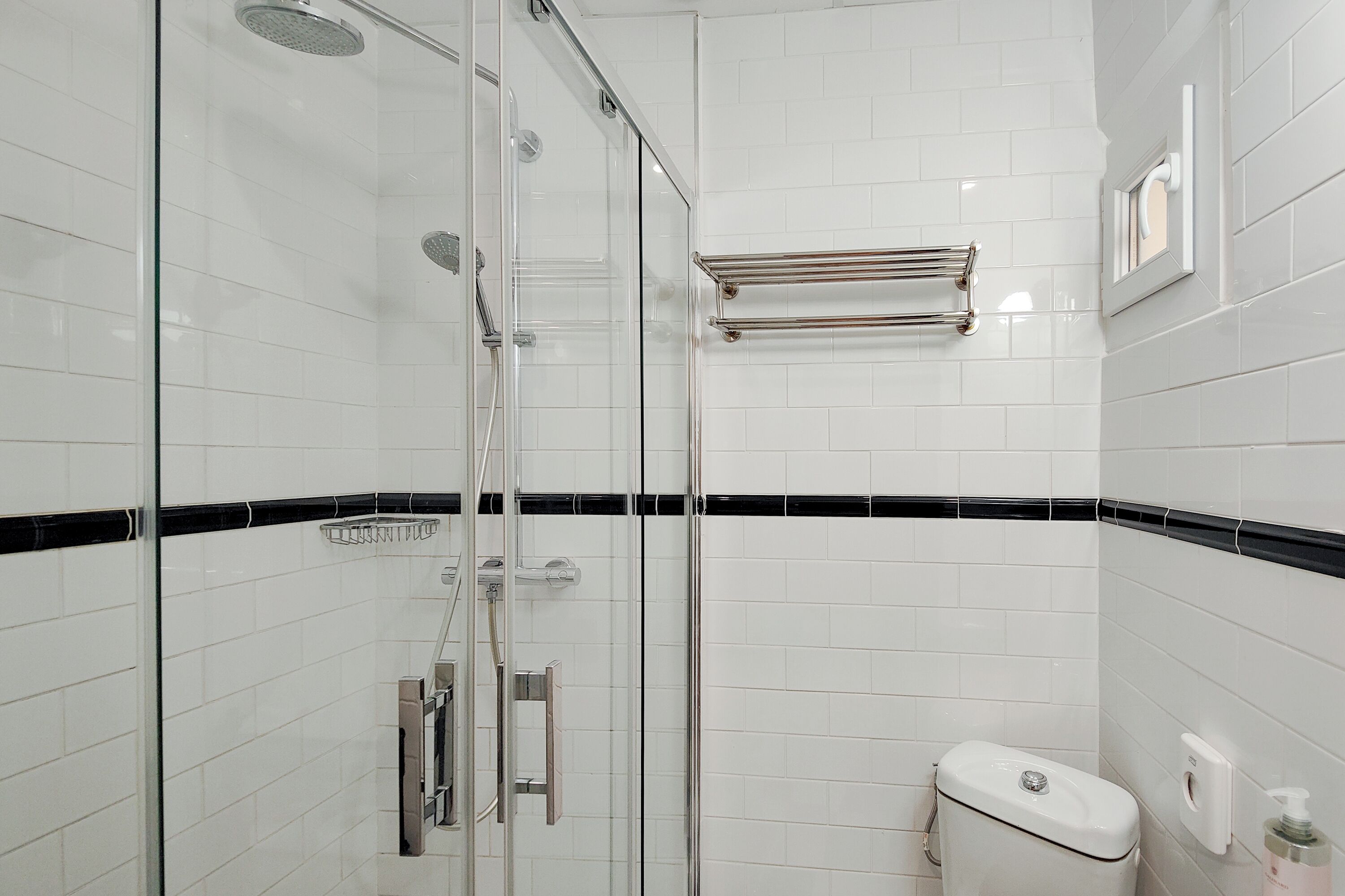 A modern bathroom with a glass-enclosed shower, white tiled walls, and a black-tiled accent strip.
