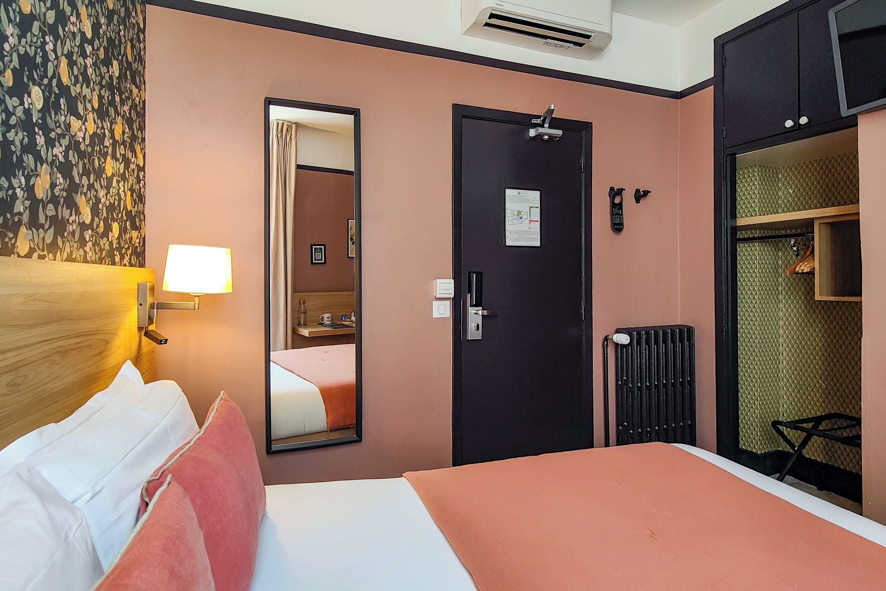 Hotellihuone, jossa on sänky, peili, ovi ja patteri.