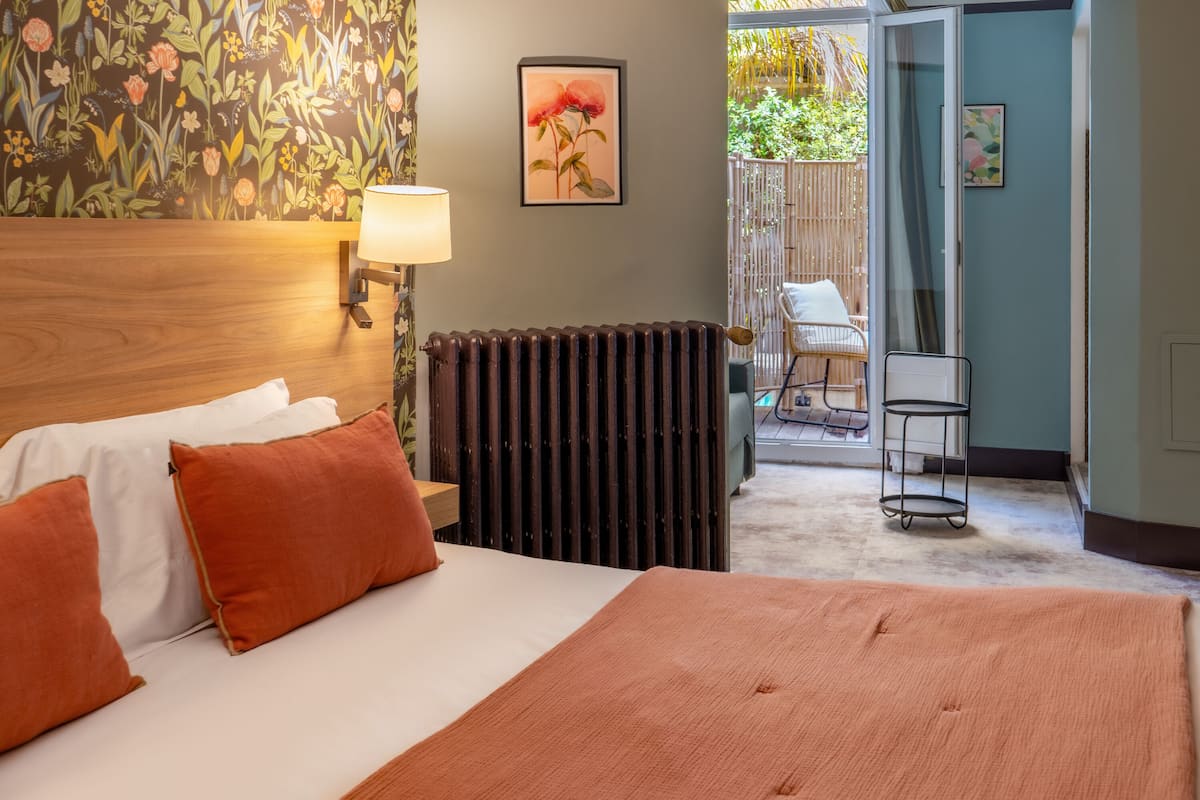 Ein Hotelzimmer mit Bett, Heizkörper, Lampe und Blick auf einen Außenbereich mit Stuhl und Tisch.