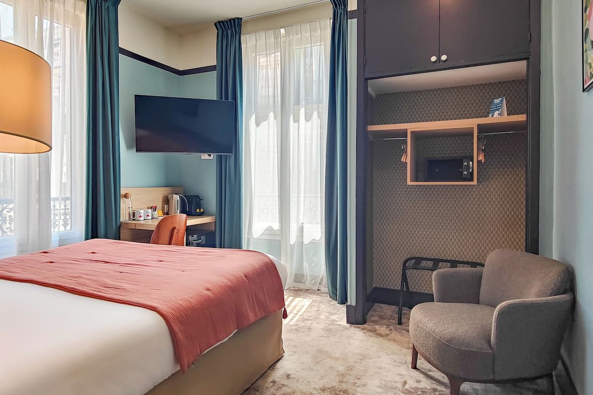 A hotel room with a bed, a desk, a chair, a TV, and a built-in shelf.