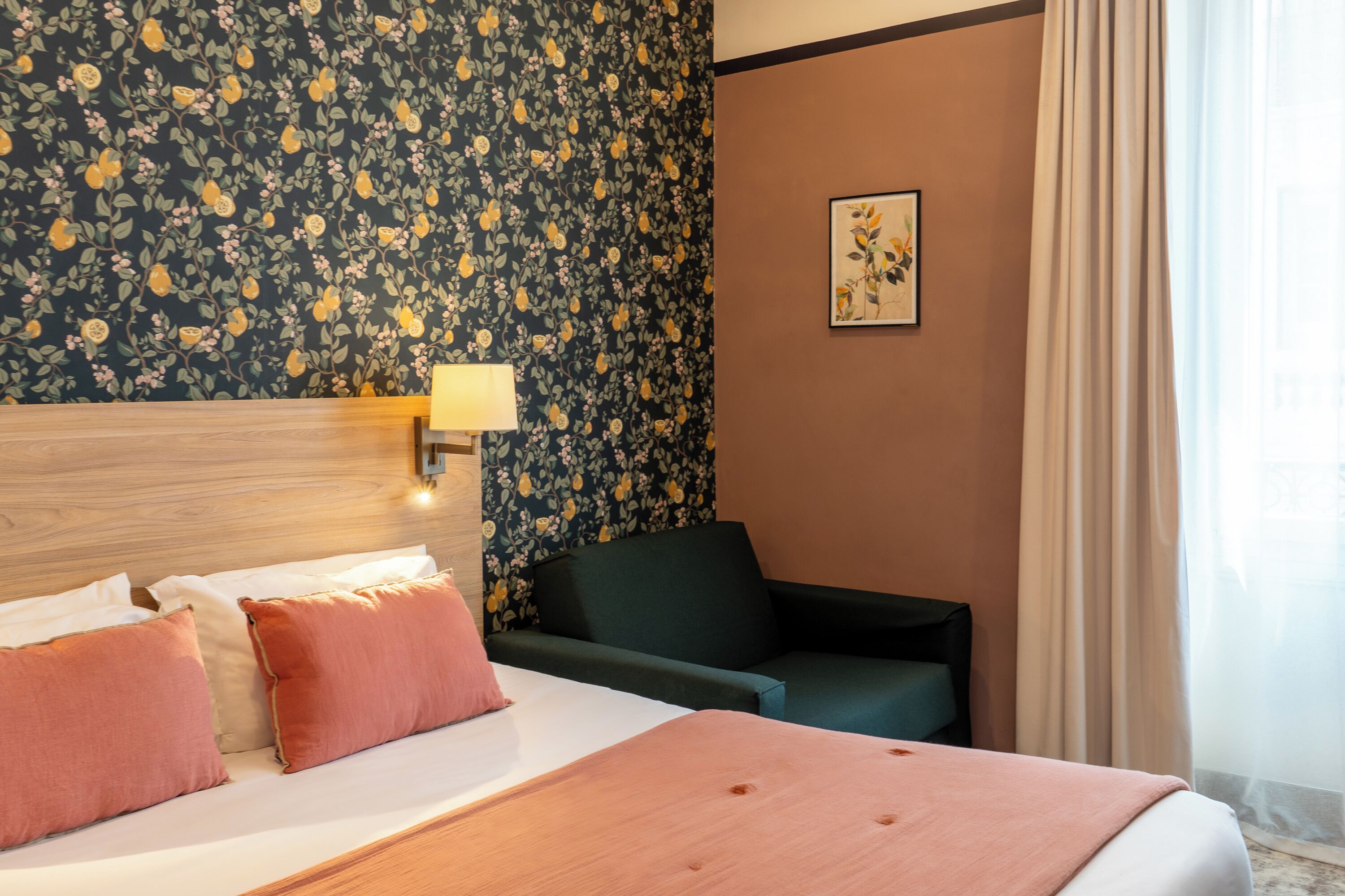 A hotel room with a bed, a nightstand, a lamp, a chair, a floral wallpaper, and a painting on the wall.